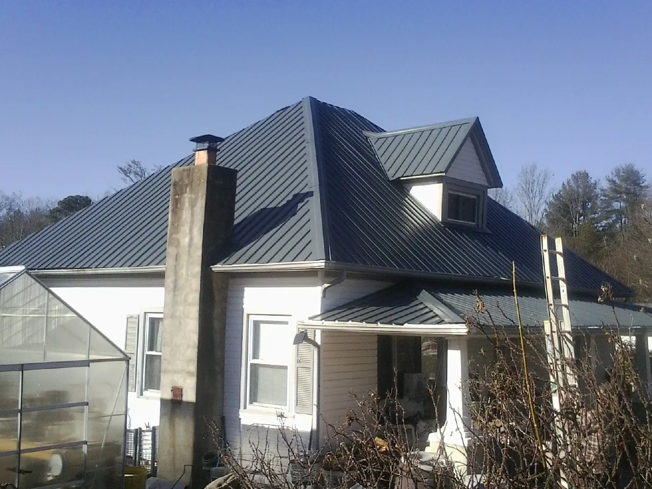 Dark blue standing seam metal roof on a white farmhouse with dormer — Slate & Tile Roof Repair by Roofing Brothers in North Baltimore