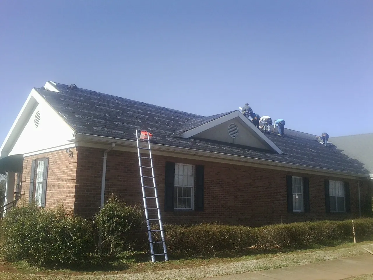 Crew tearing shingles off a brick ranch roof with a ladder set — Emergency Roof Repair work by our crew in North Baltimore