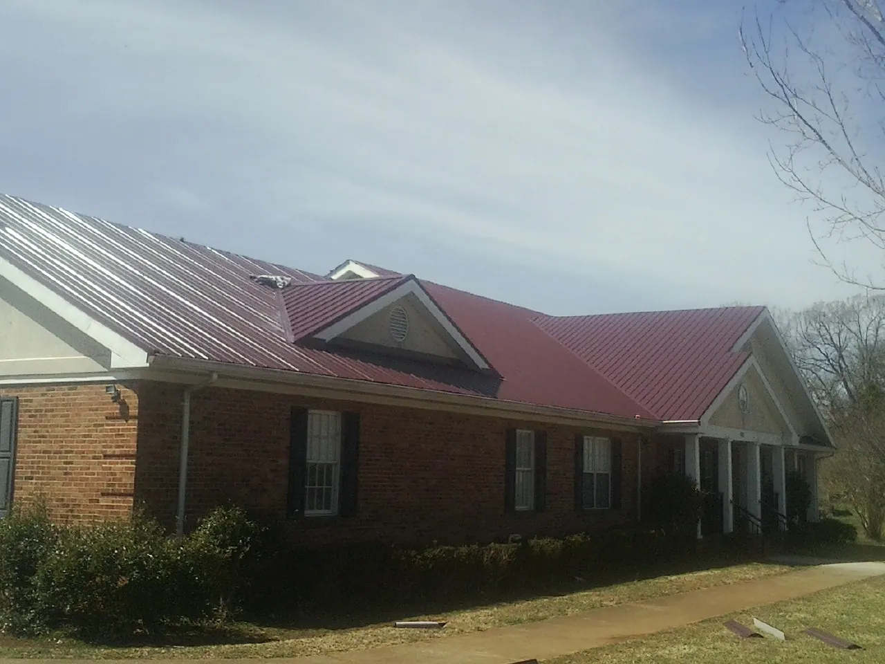 Red metal roof with gabled entries on a long brick building, from a Hail Damage Roof Repair job in North Baltimore