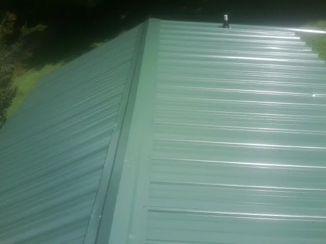 New green metal panels meeting at the ridge of a roof — Flat Roof Repair work by our crew in North Baltimore