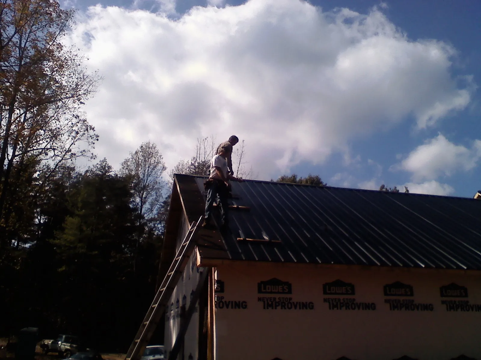 Roofer fastening dark metal panels high against a cloudy sky, from a Roof Inspection job in North Baltimore