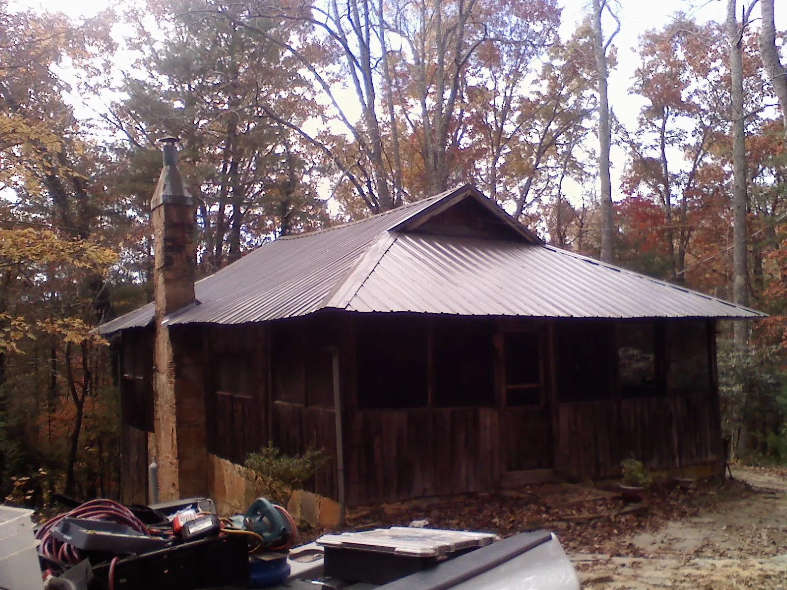 Brown metal hip roof on an old cabin with a stone chimney in North Baltimore