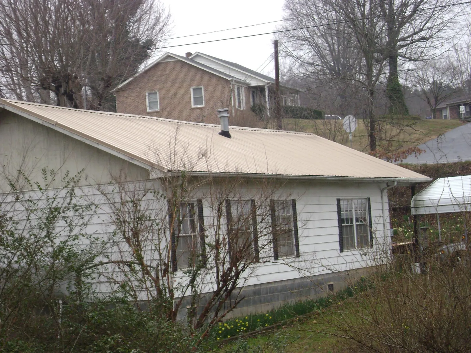 Tan metal roof on a white sided house set into a hillside — Commercial Roofing by Roofing Brothers in North Baltimore
